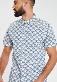 Korte mouwen, overhemd met knopen aan de voorkant in het wit met een blauw geometrisch hexagonaal patroon. Beschikt over een klassieke kraag en een gladde katoenen stof.