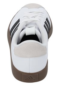 Scarpa sportiva bianca con strisce nere, dotata di una cappetta in pelle scamosciata sul tallone, superiore in tessuto testurizzato e suola in gomma marrone.