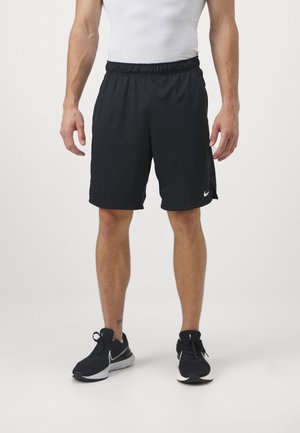 Mustat urheilushortsit, joissa on joustava vyötärö, sileä pinta ja valkoiset logoyksityiskohdat, yhdistettynä mustiin tossuihin neutraalilla taustalla.