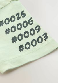 Minta vihreä lyhythihainen paita, jossa on suuret mustat numerot ja hashtagit printattuna hihaan. Pehmeää kangasta ja rento istuvuus.