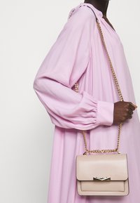 Borsa a mano rosa chiaro con tracolla a catena dorata, forma rettangolare, texture in pelle liscia e dettaglio in metallo sulla parte frontale.