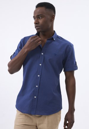 Camisa azul de manga corta con botones, hecha de tela ligera, que presenta un logo sutil, botones blancos en contraste y puños enrollados.