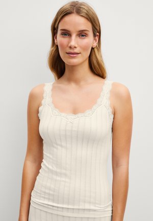 Woman with light brown hair wearing a cream-colored ribbed tank top with lace trim on the neckline and straps.