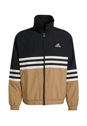 Zwarte, tan en witte windbreaker jas met een hoge kraag, rits aan de voorkant, witte strepen op de mouwen en een adidas-logo op de borst.