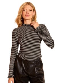 Fekete-fehér csíkos hosszú ujjú felső fodros gallérral és testhezálló szabással, magas derekú fekete bőrnadrággal párosítva.