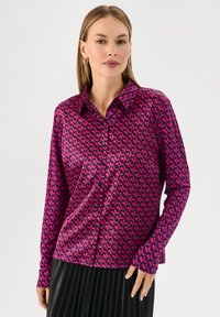 Camicia a maniche lunghe in tessuto simil-seta fucsia con un motivo curvo ripetitivo in rosa scuro, dotata di chiusura con bottoni e colletto.