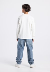 Long-sleeve white cotton shirt with a crew neckline, paired with light blue denim cargo pants featuring side pockets and a relaxed fit.