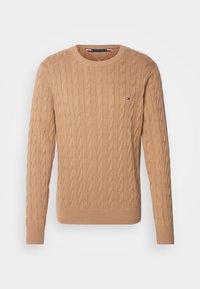 Pull beige en maille torsadée à col rond, manches longues, avec un petit logo Tommy Hilfiger sur le côté gauche de la poitrine.