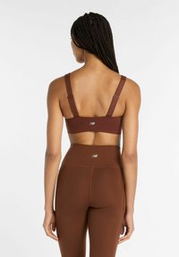 Brun sport-bh och högmidjade leggings i slät tyg. Båda har en minimalistisk design med logotypdetaljer.