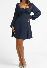 Granatowa sukienka z kwadratowym dekoltem, marszczonym biustem, długimi rękawami i rozkloszowanym dołem. Tkana tkanina z detalami w postaci guzików.