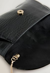 Clutch in pelle sintetica nera effetto coccodrillo con texture liscia, chiusura con bottone magnetico e ferrature dorate all'interno. L'interno presenta una fodera in tessuto nero.