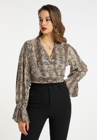 Afskåret bluse med slangeprint i beige og brun, med lange ærmer med flæser, parret med højtsiddende sorte bukser.