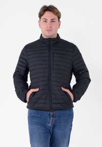 Zwarte gestepte pufferjack met een hoge kraag, een ritssluiting aan de voorkant en zijzakken. Het materiaal lijkt lichtgewicht met een gladde textuur.