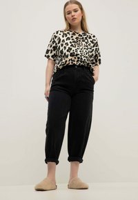 Top corto a fantasia leopardata, pantaloni neri a vita alta con orli arrotolati e scarpe beige fluffy slip-on. Tessuto morbido, vestibilità casual.