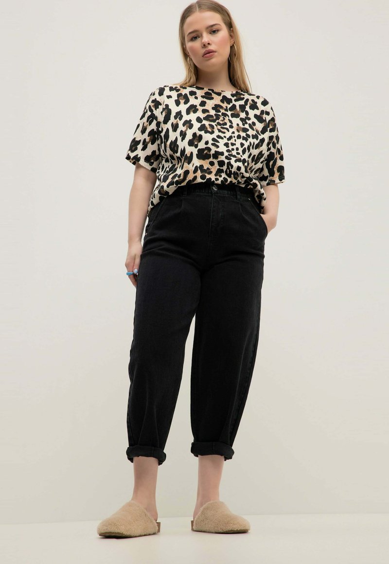 Top corto a fantasia leopardata, pantaloni neri a vita alta con orli arrotolati e scarpe beige fluffy slip-on. Tessuto morbido, vestibilità casual.