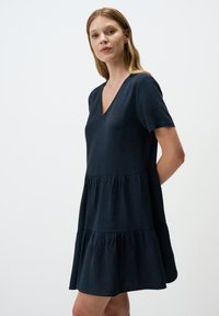 Ciemnoniebieska sukienka w kroju A z lekkiego materiału, z dekoltem w serek, krótkimi rękawami i falbanowym różnorodnym dołem. Gładka tekstura, luźny krój.