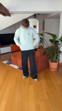 Sweatshirt com capuz azul claro com um logótipo, calças pretas de perna larga e sapatos prateados. Roupa casual com materiais macios e corte descontraído.