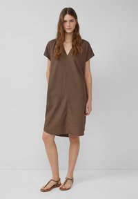 Robe en lin marron avec un col en V, des manches courtes et une coupe ample. Le design comporte une couture centrale et arrive au milieu de la cuisse.