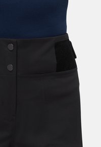 Μαύρο παντελόνι με υφασμάτινη μέση, δύο μεταλλικά κουμπιά μπροστά και μία πλάγια τσέπη με αντίθετο υφασμάτινο πάνελ.