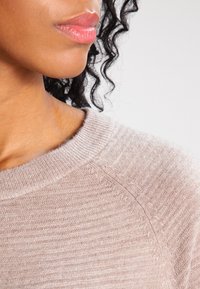 Pull en maille beige clair avec une finition texturée, doté d'un col rond côtelé et de manches raglan, offrant un look confortable et décontracté.