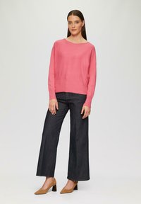 Roze, geribbelde sweater met een ronde halslijn, gecombineerd met donkere, wijde jeans en tan, puntige hakken, tegen een neutrale achtergrond.
