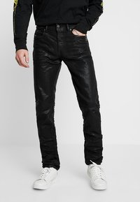 Svart denimjeans med slim fit, med subtila slitna områden och en mjuk textur, ihop med vita sneakers och en svart långärmad tröja.