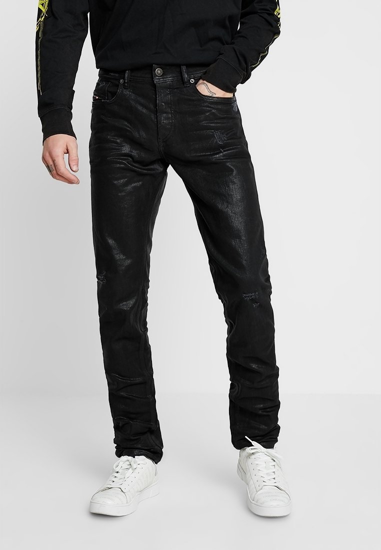 Svart denimjeans med slim fit, med subtila slitna områden och en mjuk textur, ihop med vita sneakers och en svart långärmad tröja.