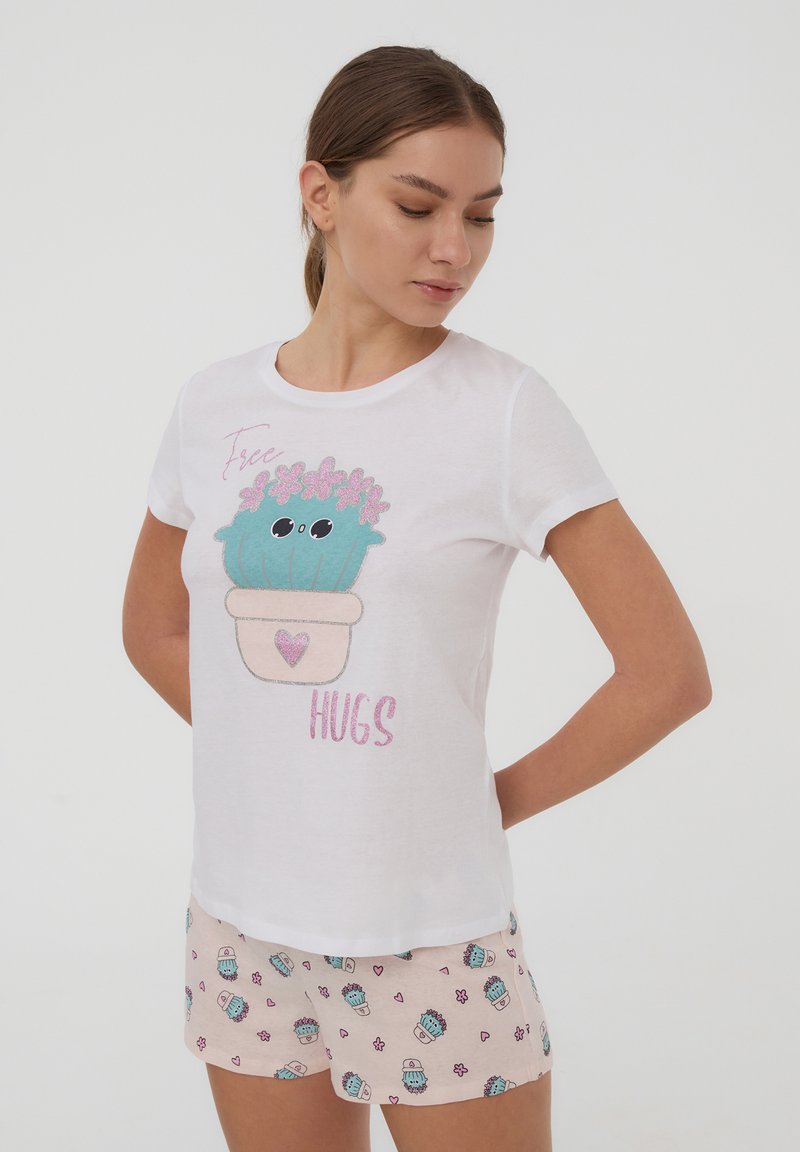 Maglietta bianca a maniche corte con una grafica di un cactus cartoon in un vaso con fiori rosa e la scritta "Abbracci gratis". Pantaloni corti a fantasia rosa.