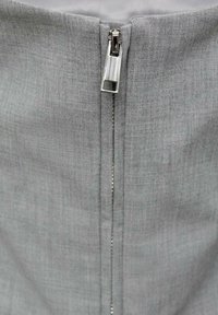 Grå tygväska med en slät, texturerad yta, med en central metalldragkedja och en rektangulär dragtab högst upp.