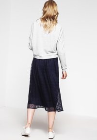 Sudadera gris cortada con hombros caídos combinada con una falda midi plisada azul marina. El conjunto se completa con zapatillas blancas.