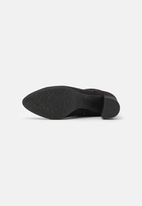 Schwarze Wildleder-Stiefelette mit einer glatten Gummisohle. Texturiertes Muster auf der Sohle für besseren Grip. Seitlicher Reißverschluss, leicht erhöhter Absatz.