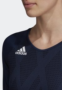 Marinblå sporttopp med ett mönster, rund halsringning och broderad vit Adidas-logotyp på vänster axel.