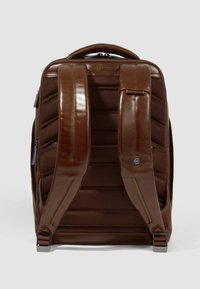 Mochila marrón con correas de cuero lisas y un cuerpo texturizado. Presenta un respaldo acolchado, correas ajustables y cierre de cremallera.