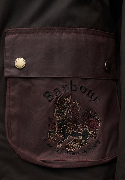 Τσέπη από σκουρό καφέ ύφασμα με κεντητό λογότυπο Barbour, σχέδιο μυθικού πλάσματος και κουμπιά με κλιπ σε ένα μπουφάν.