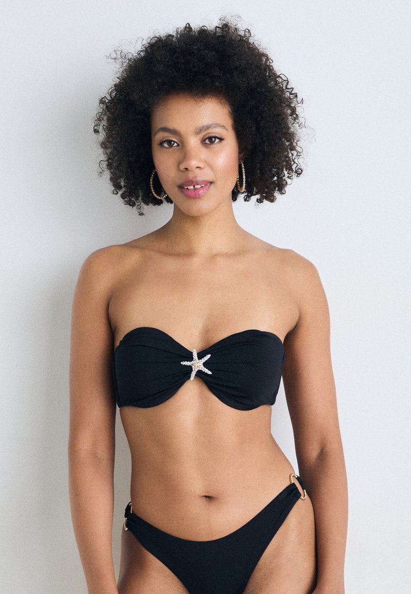 Fekete bikini, bandeau felsővel, amely csavart dizájnnal és tengeri csillag díszítéssel rendelkezik. Az alsó részen oldalsó gyűrűk találhatók, klasszikus szabású. Simább text�úra.
