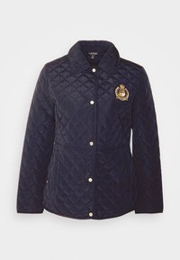 Vadderad marinblå jacka med krage, guldfärgade knappar och ett emblem med vapenmärke. Den har en texturerad yta och framfickor.