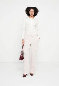 Weißes Langarmshirt mit Knopfleiste, kombiniert mit weit geschnittenen, hellrosa Hosen mit Kordelzug. Dunkelroter Handtasche und Absatzschuhe.