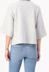 Maglione morbido grigio chiaro a maglia con scollatura arrotondata e maniche larghe, abbinato a jeans blue denim con tasche posteriori standard.
