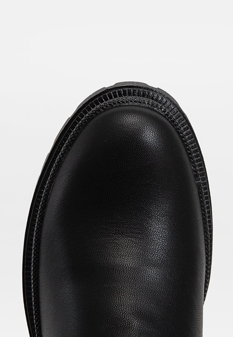 Punta di un stivaletto in pelle nera con cuciture dettagliate e bordo della suola testurizzato, vista dall'alto in primo piano.
