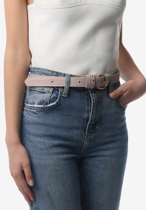 Lyserød læderbælte med krokodillemønster og en gylden cirkulær spænde. Bæltet bæres over højtaljede blå denimjeans. Struktureret overfladedetalje synlig.