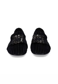 Zapatos de lona negros con suela plana, que presentan una hebilla decorativa y textura acanalada horizontal.