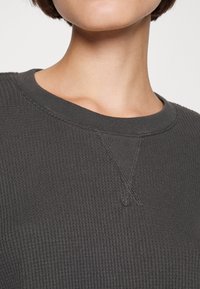 Maglione a coste grigio scuro con collo a girocollo e leggero dettaglio a V sul colletto, che mette in risalto la texture e le lavorazioni di cucitura.