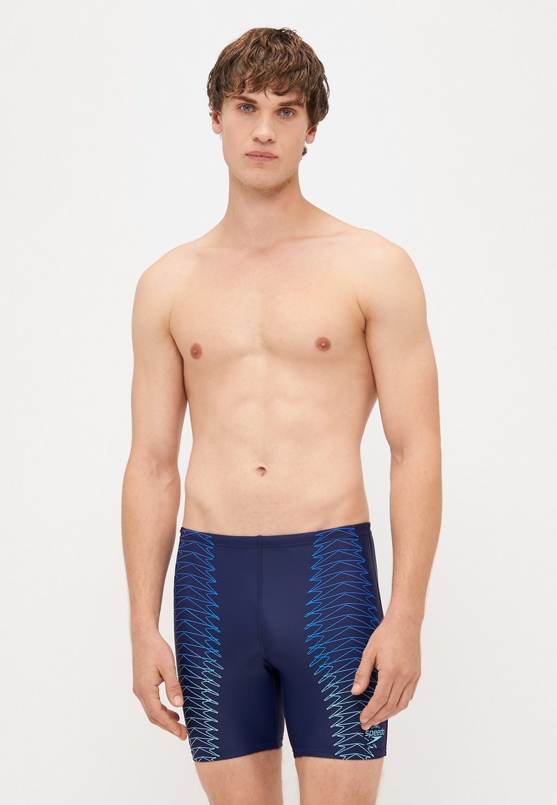 Ναυτικά μαγιό φτιαγμένα από ελαστικό υλικό, με μπλε σχέδιο ζιγκ-ζαγκ στα πλευρά και εφαρμοστή γραμμή.