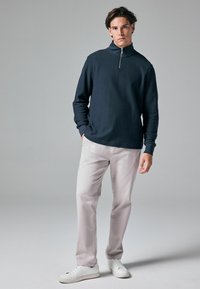 Marinefarbener Reißverschluss-Pullover aus strukturiertem Stoff, kombiniert mit hellen Chinos und weißen Sneakers. Schlichtes, modernes Design mit bequemer Passform.