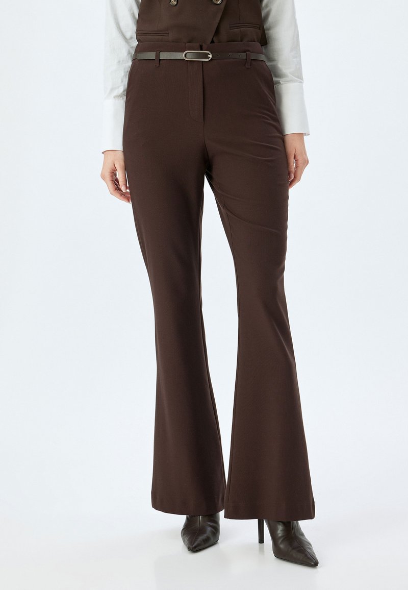 Bruine uitlopende trousers met een soepele textuur, voorzien van een riem met metalen gesp, een getailleerde pasvorm en een hoge taille, gecombineerd met puntige hakken.