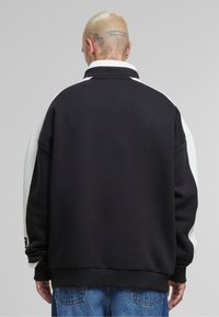 Sort og hvid oversized sweatshirt med krave, der har et tekstureret stof, farveblokkerede ærmer og ribbede manchetter.