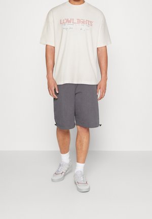 Herre cremede oversized t-shirt med trykt tekst, parret med grå shorts. Sneakers med diskrete detaljer. Blødt bomuldsmateriale, afslappet pasform.