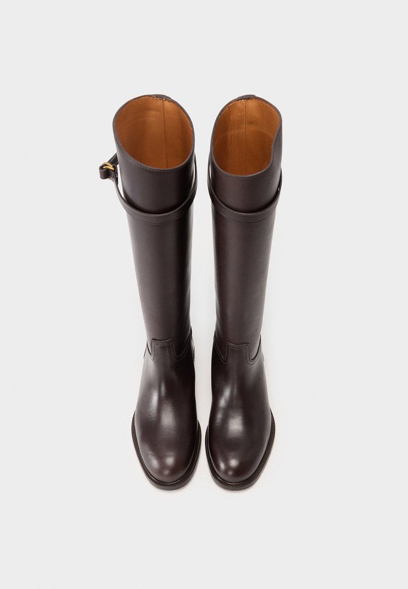 Brązowe skórzane kozaki do kolan o gładkiej powierzchni, zaokrąglonym nosku i ozdobnym przeszyciu przy kostce. Posiadają wewnętrzny zamek błyskawiczny i detal w postaci paska.