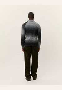 Pulover tricotat într-un gradient de nuanțe de gri, cu un design ajustat și mansete cu nervuri. Asociat cu pantaloni din catifea de culoare verde închis.