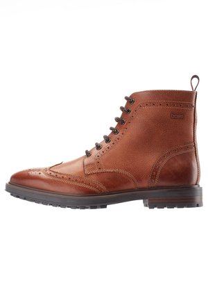 Bota baja de cuero marrón con diseño brogue y ala decorativa, suela de goma negra y lengüeta en el talón, vista lateral.